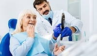 a woman looking at her new teeth in a mirror at the dental office