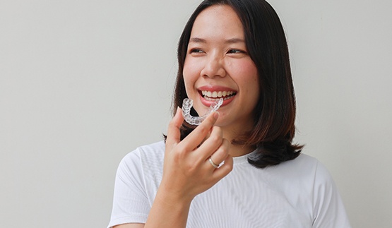 Smiling patient holding clear aligner