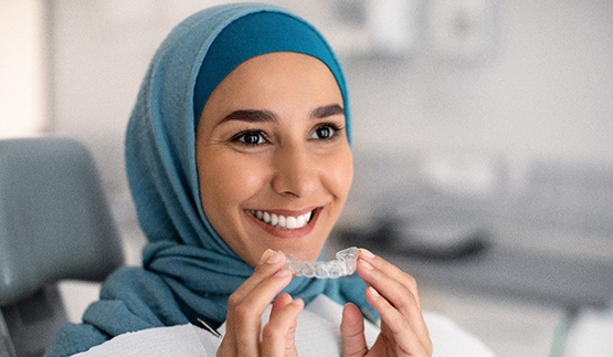 Woman smiling while holding clear aligner in treatment room