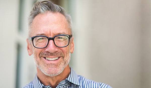 Older man in collared shirt wearing glasses and smiling