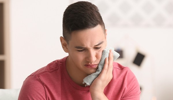 Young man who needs emergency dentist in Collinsville holding a cold compress to his jaw