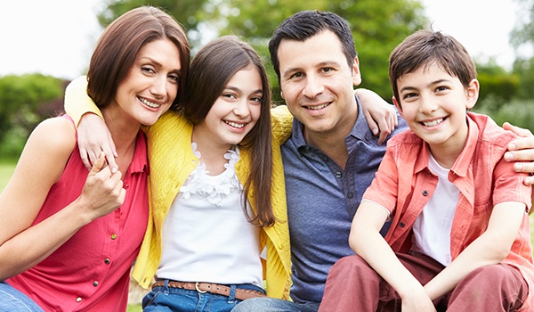 Smiling family of four sitting outdoors after visiting their family dentist in Collinsville