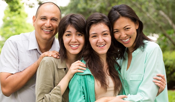 Family of four smiling outdoors after visiting their Collinsville dentist