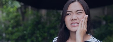 Woman holding her cheek in pain while outdoors
