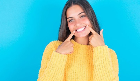 Woman in yellow sweater pointing at her white teeth