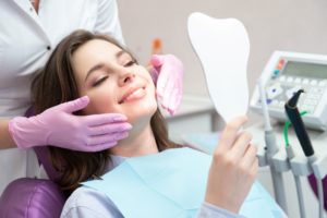 Woman sitting in dental chair looking into a mirror while a dentist with purple gloves stands behind her