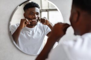 Young man looking in the mirror while flossing his teeth.